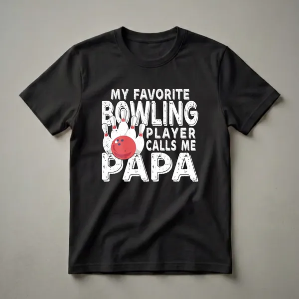 Black t-shirt with white distressed text that reads 'MY FAVORITE BOWLING PLAYER CALLS ME PAPA' and graphics of a red bowling ball and white pins.