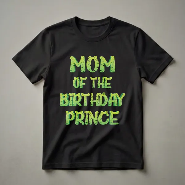 Green graphic t-shirt with the words 'Mom Of The Birthday Prince' in a frog-like font, set against a black background.