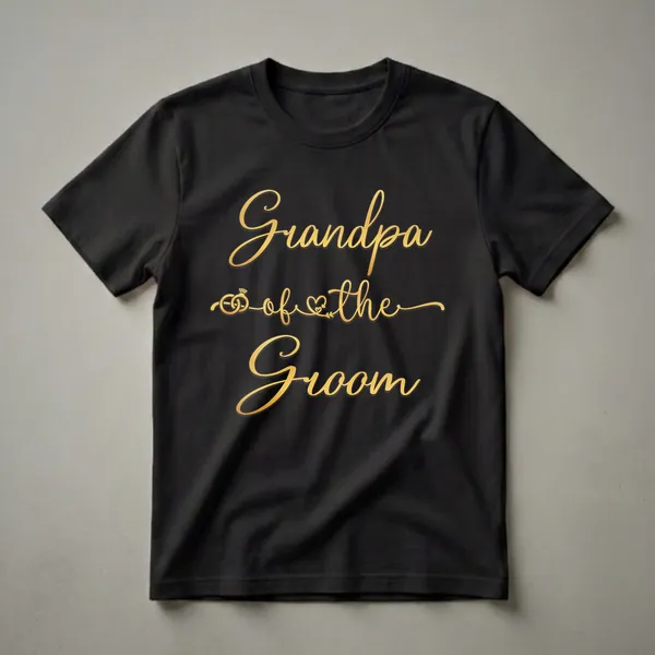 Black t-shirt with gold script text reading 'Grandpa of the Groom' and graphics of wedding rings and a heart.