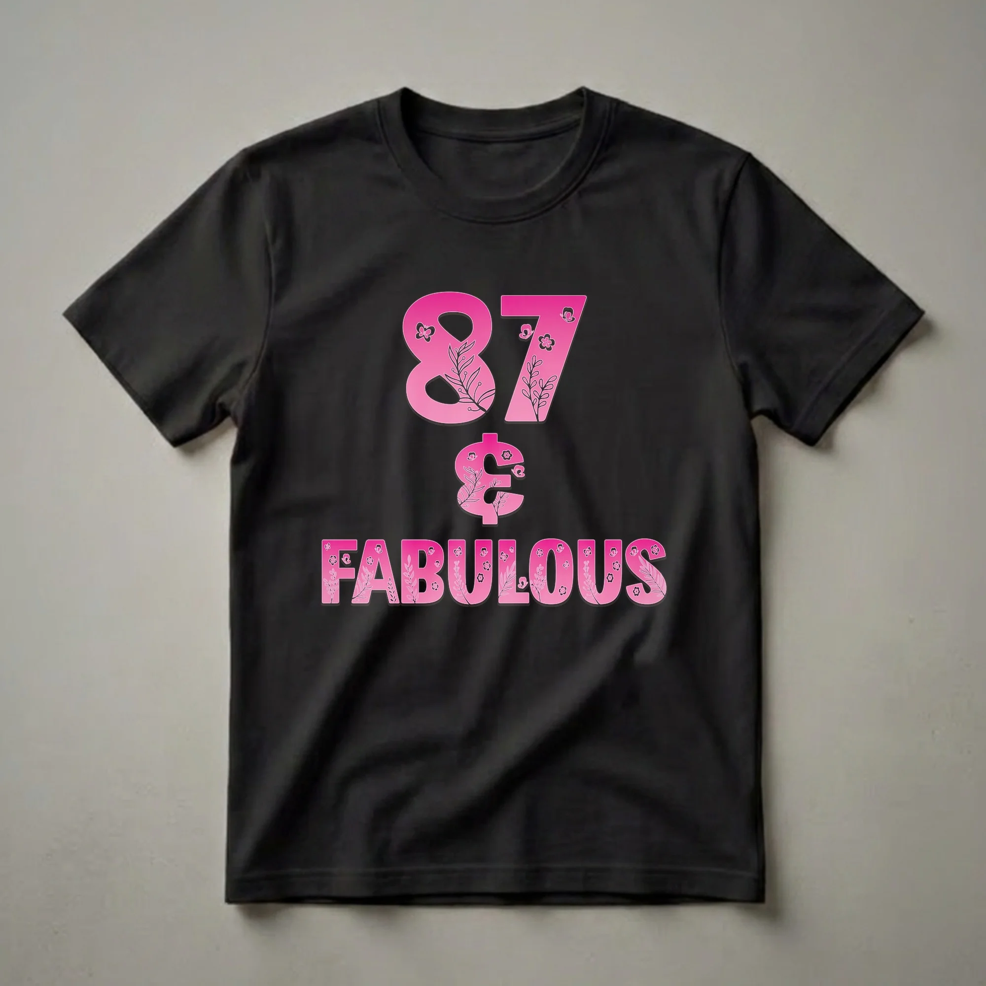 Pink graphic t-shirt with the numbers '87' and the word 'FABULOUS' decorated with floral branches and butterflies, on a black background.
