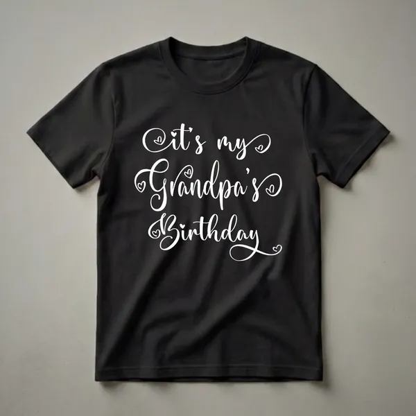 White cursive text on a black t-shirt reads 'It's my Grandpa's Birthday' with small heart accents.