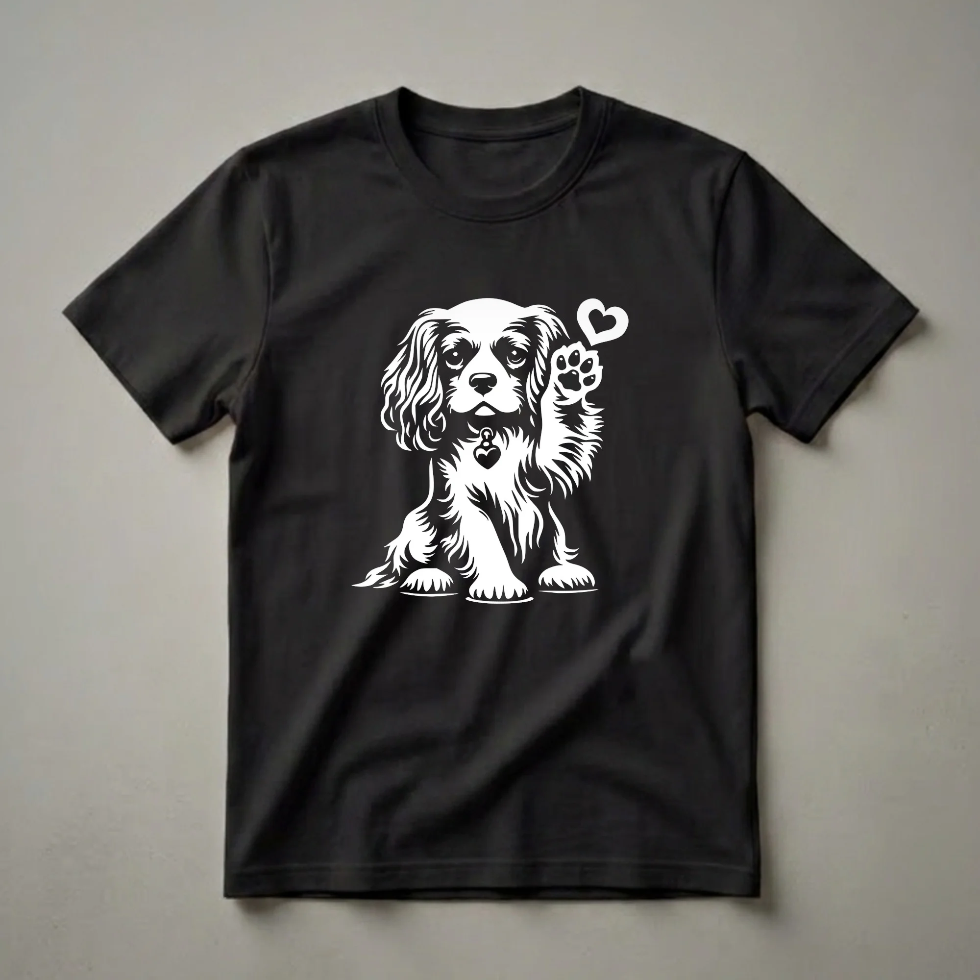 White graphic of a Cavalier King Charles Spaniel dog sitting with its paw raised, a heart symbol above it, and a heart-shaped tag on its collar, displayed on a black t-shirt.