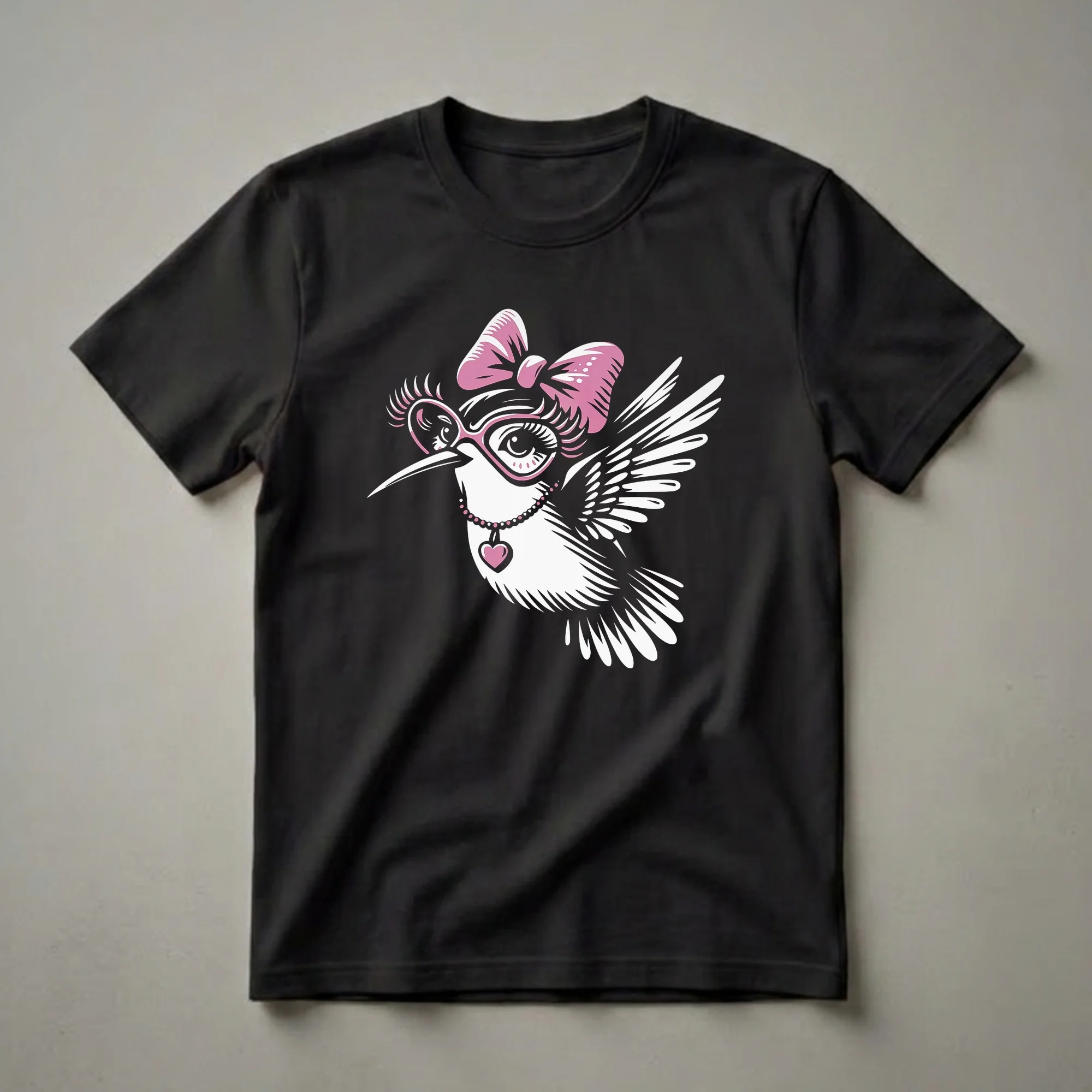 Black t-shirt featuring a white and pink graphic of a hummingbird wearing a pink bow, pink heart-shaped glasses, and a pink heart pendant necklace.