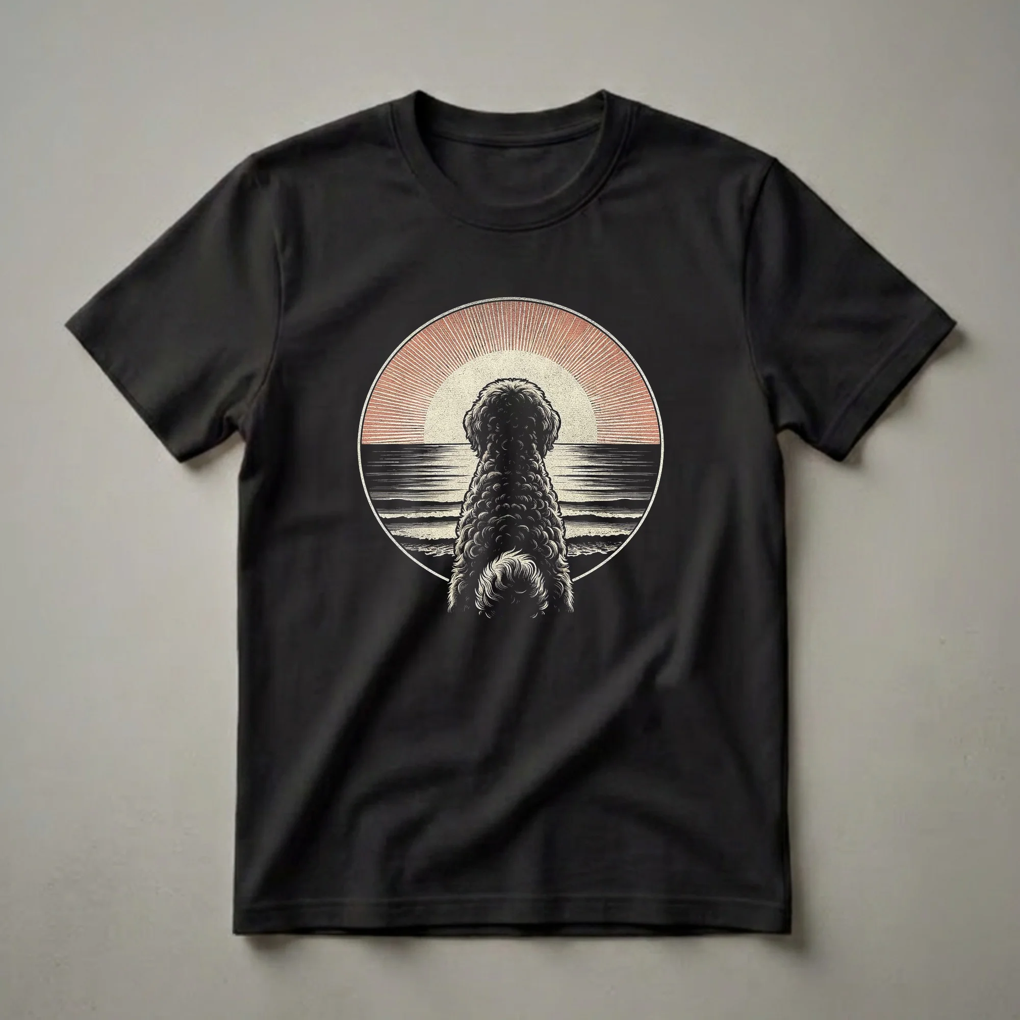 Black graphic t-shirt featuring a vintage-style illustration of a Labradoodle dog facing a retro sunset over the ocean.