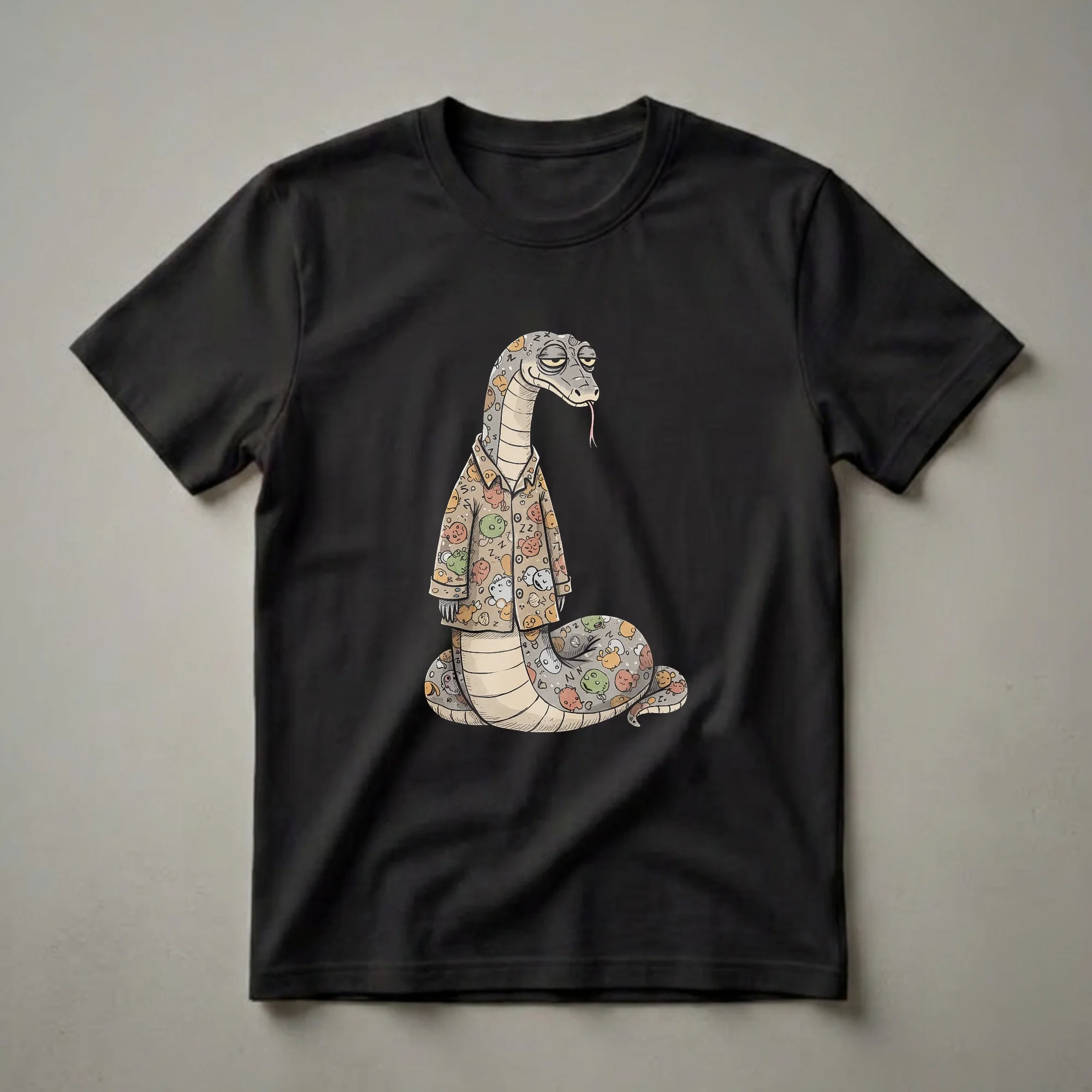 A light brown t-shirt featuring a cartoon snake wearing pajamas with a pattern of sleepy faces, moons, stars, and ZZZs, against a black background.