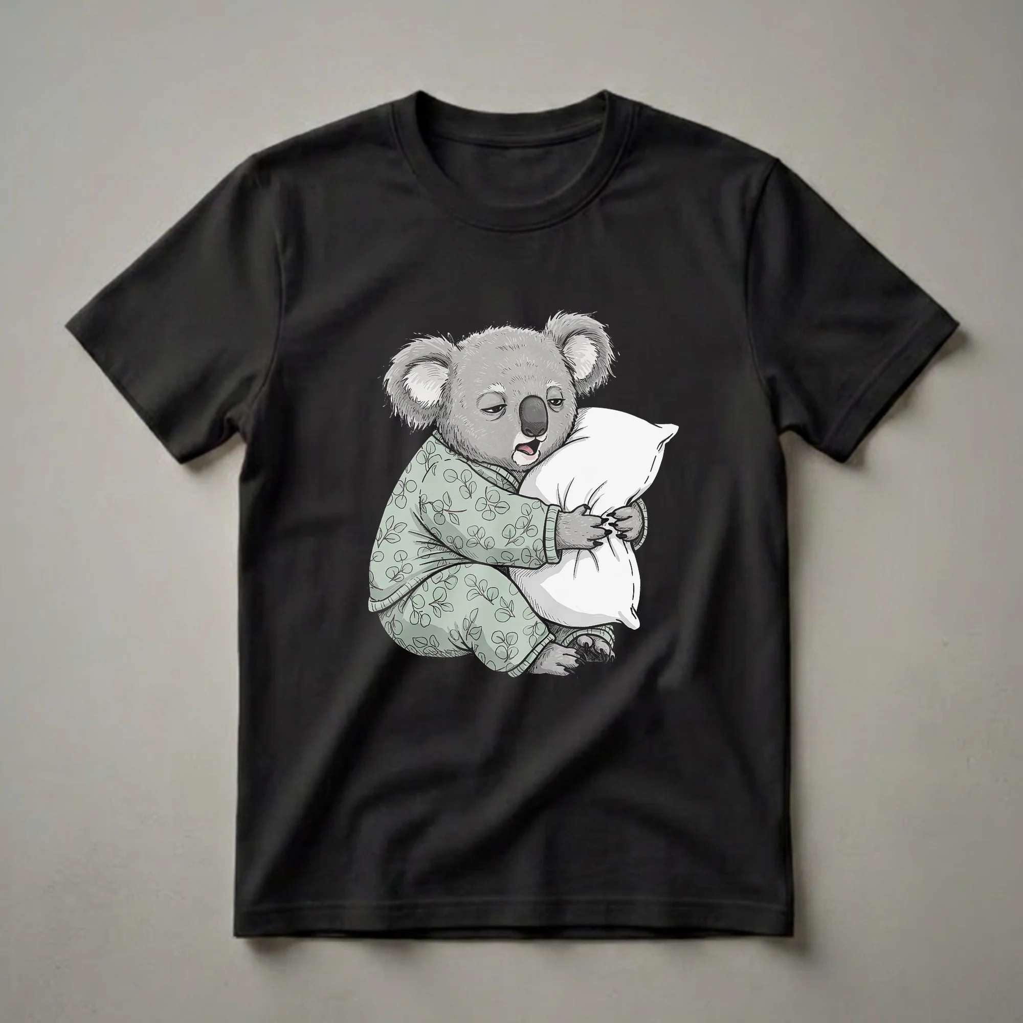 Light green graphic t-shirt featuring a cartoon koala wearing pajamas and hugging a white pillow, with a sleepy expression.