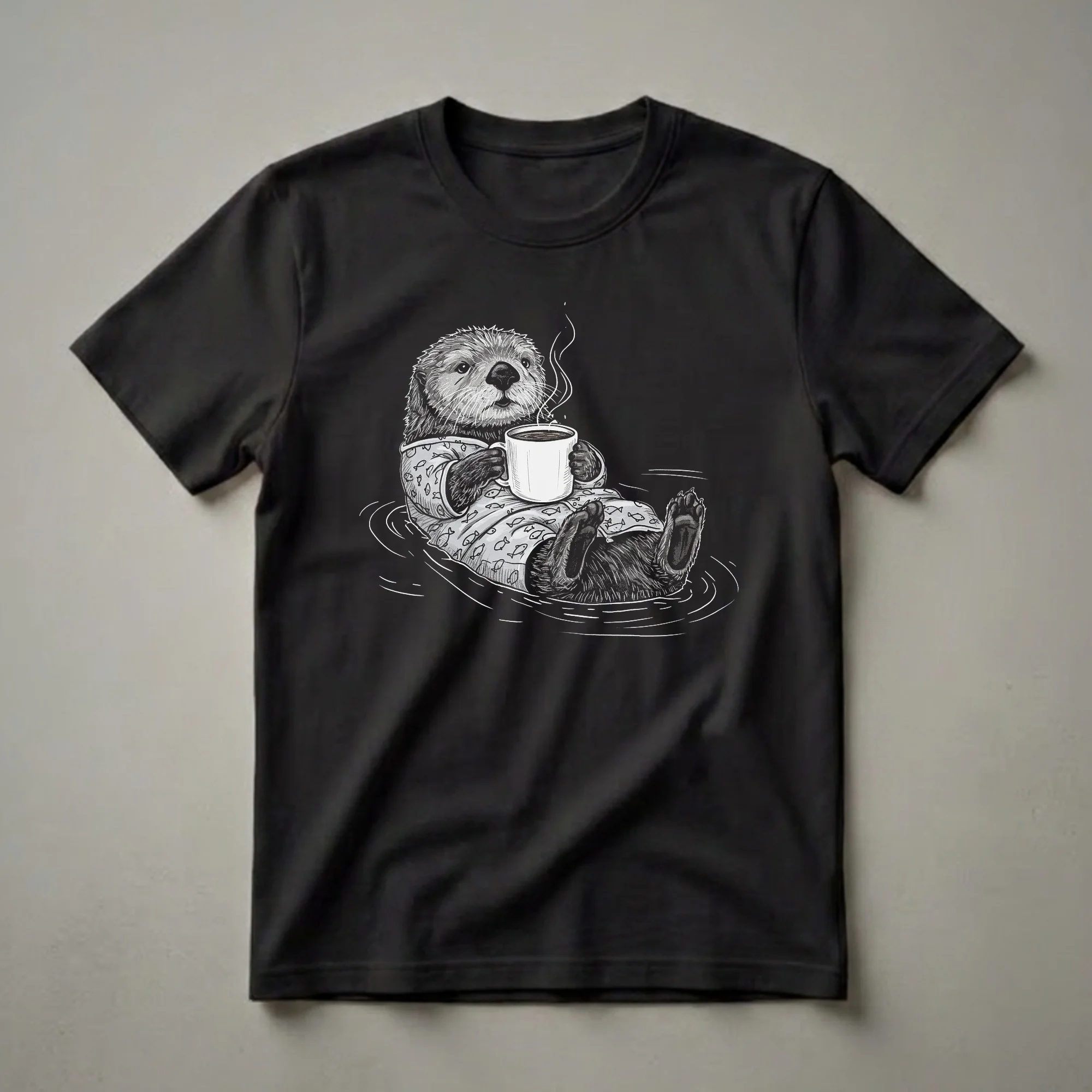 Black and white graphic t-shirt featuring a sea otter floating on its back, wearing fish-patterned pajamas and holding a steaming mug of coffee.