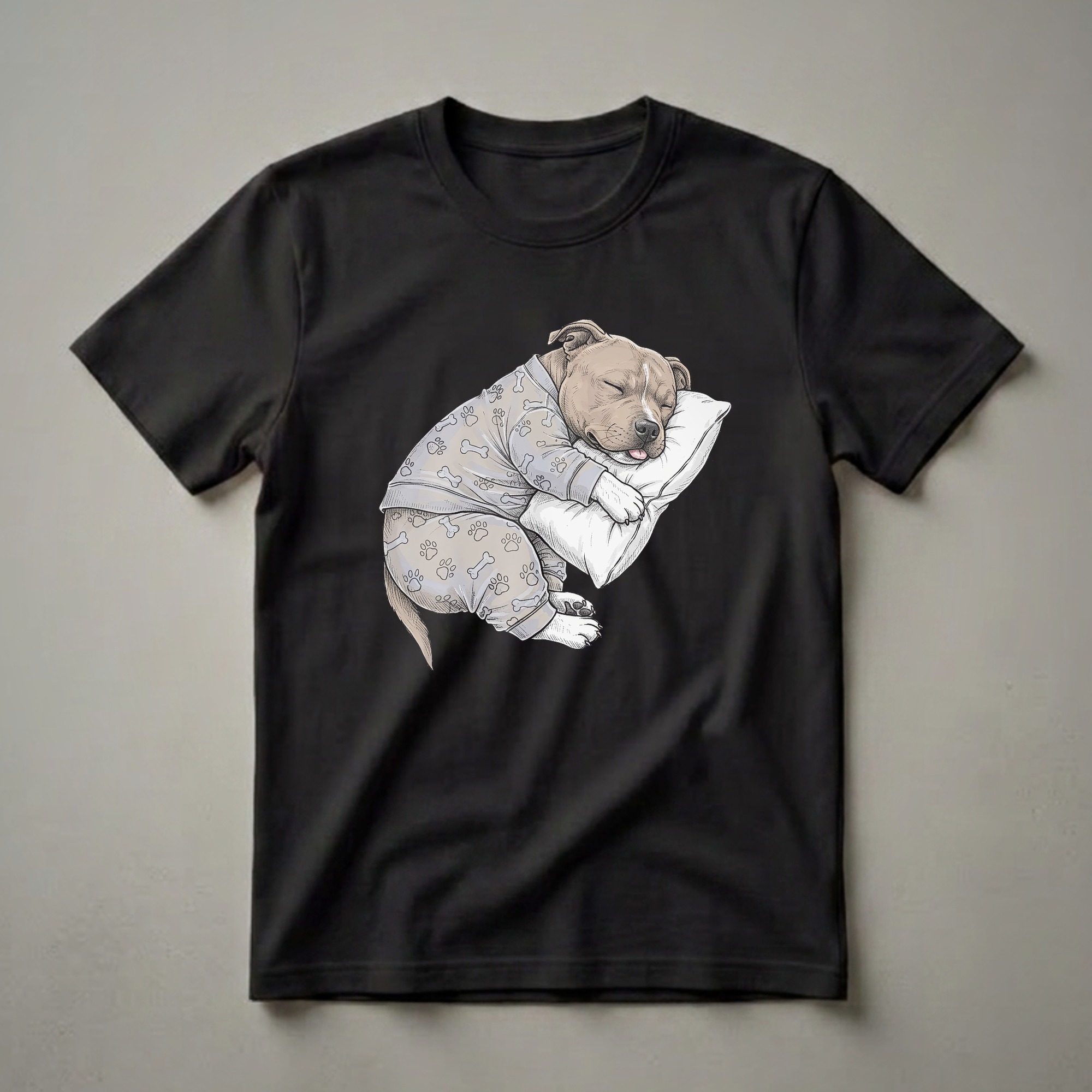 Light grey t-shirt featuring a hand-drawn illustration of a tan Staffordshire Bull Terrier puppy sleeping on a white pillow, wearing grey pajamas with paw print and bone patterns.