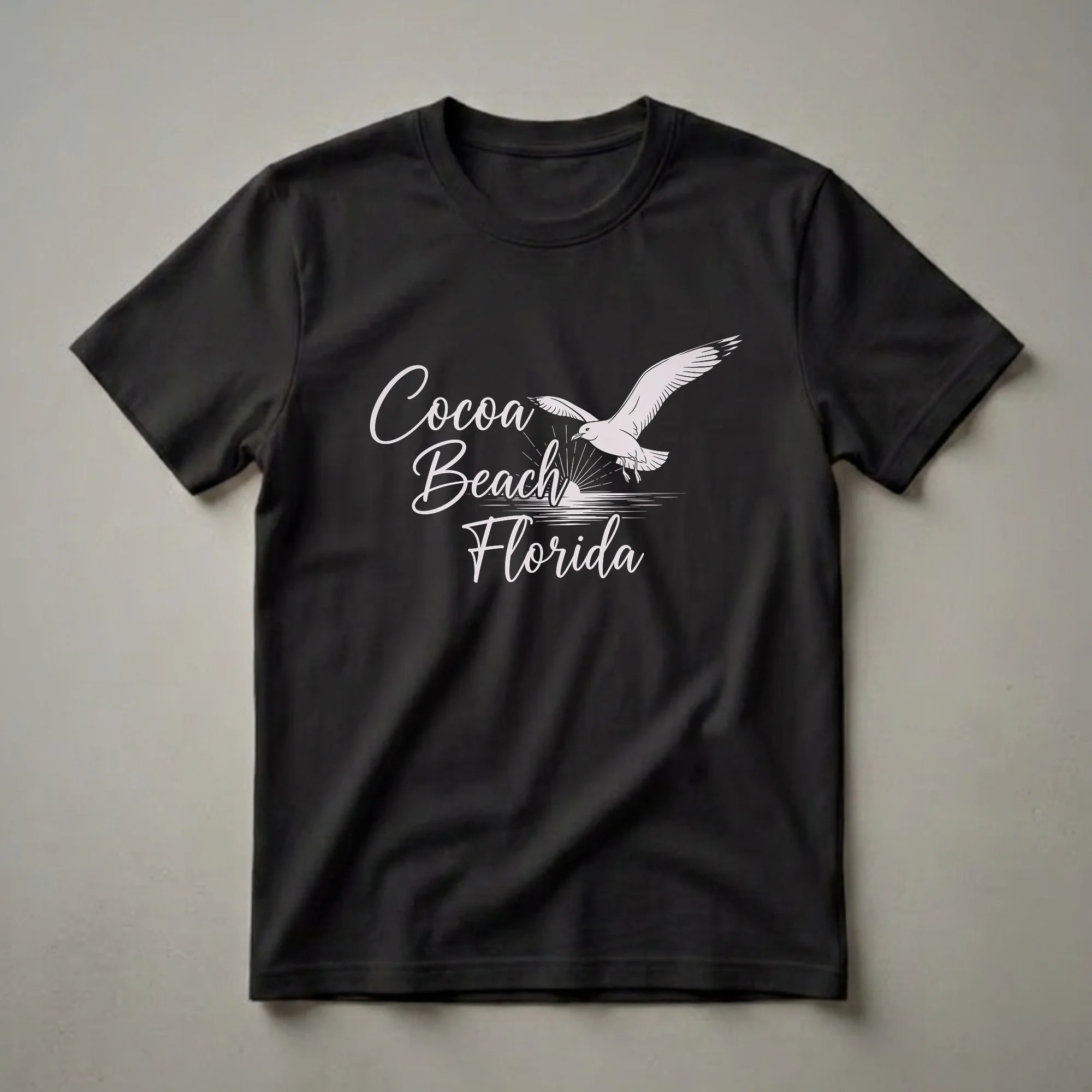 Black t-shirt with a graphic design of a seagull flying over a sunrise and water, with the text 'Cocoa Beach Florida' in script.