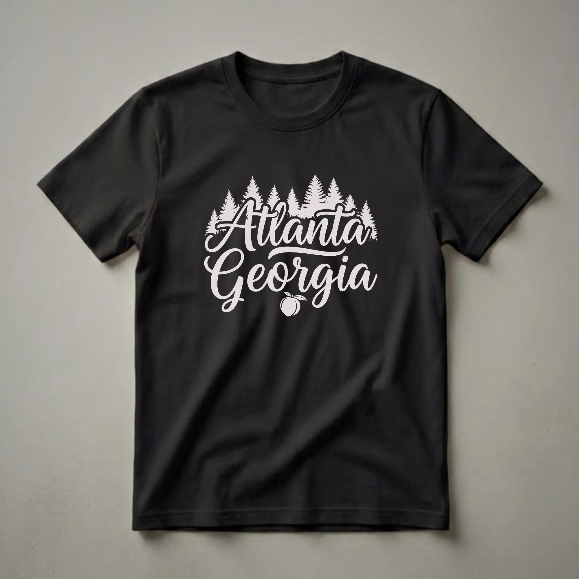 Black t-shirt with 'Atlanta Georgia' in light pink script, a peach graphic below, and a silhouette of pine trees across the top.