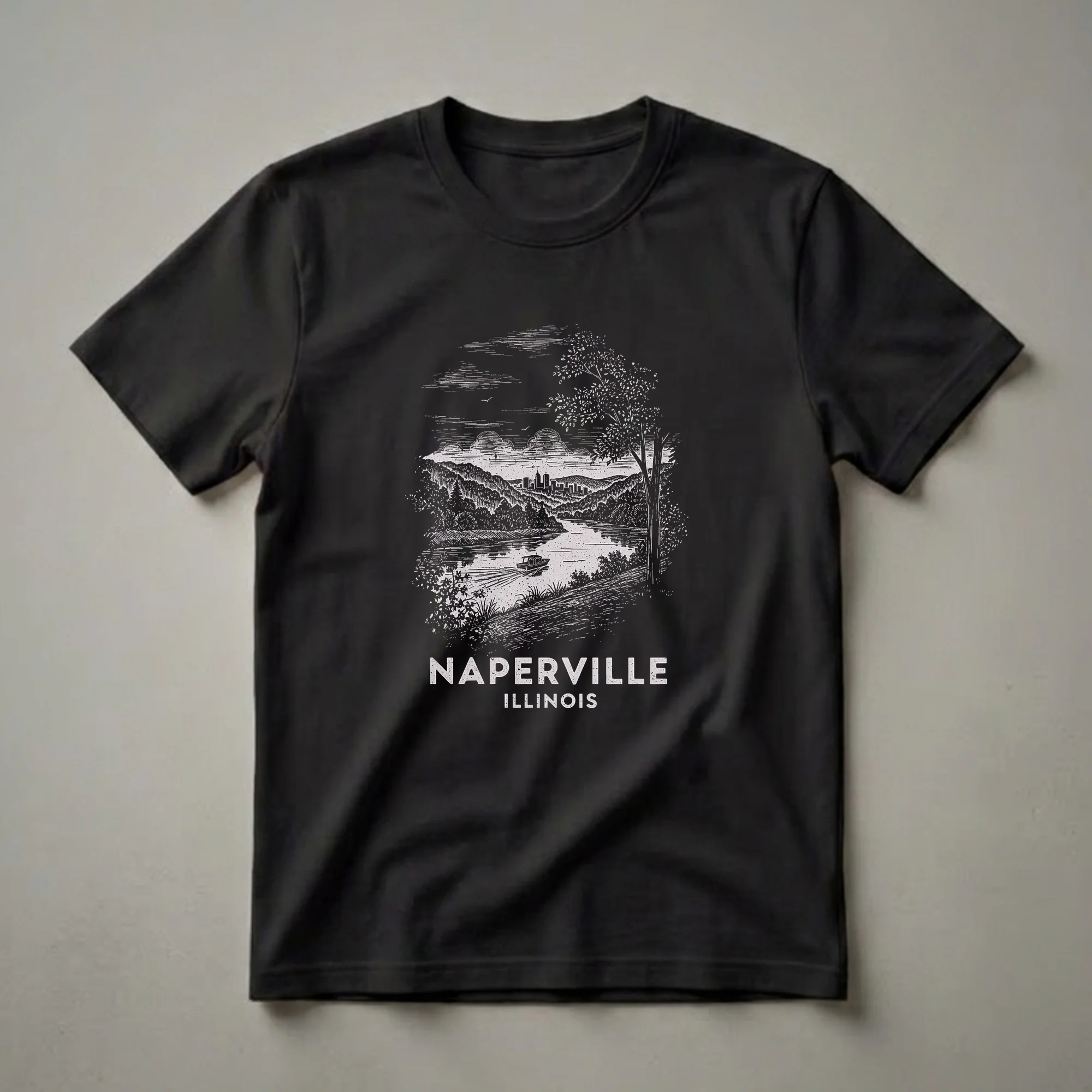 Black t-shirt with a vintage drawing of Naperville, Illinois, showing a river, boat, trees, hills, and city skyline, with text below.