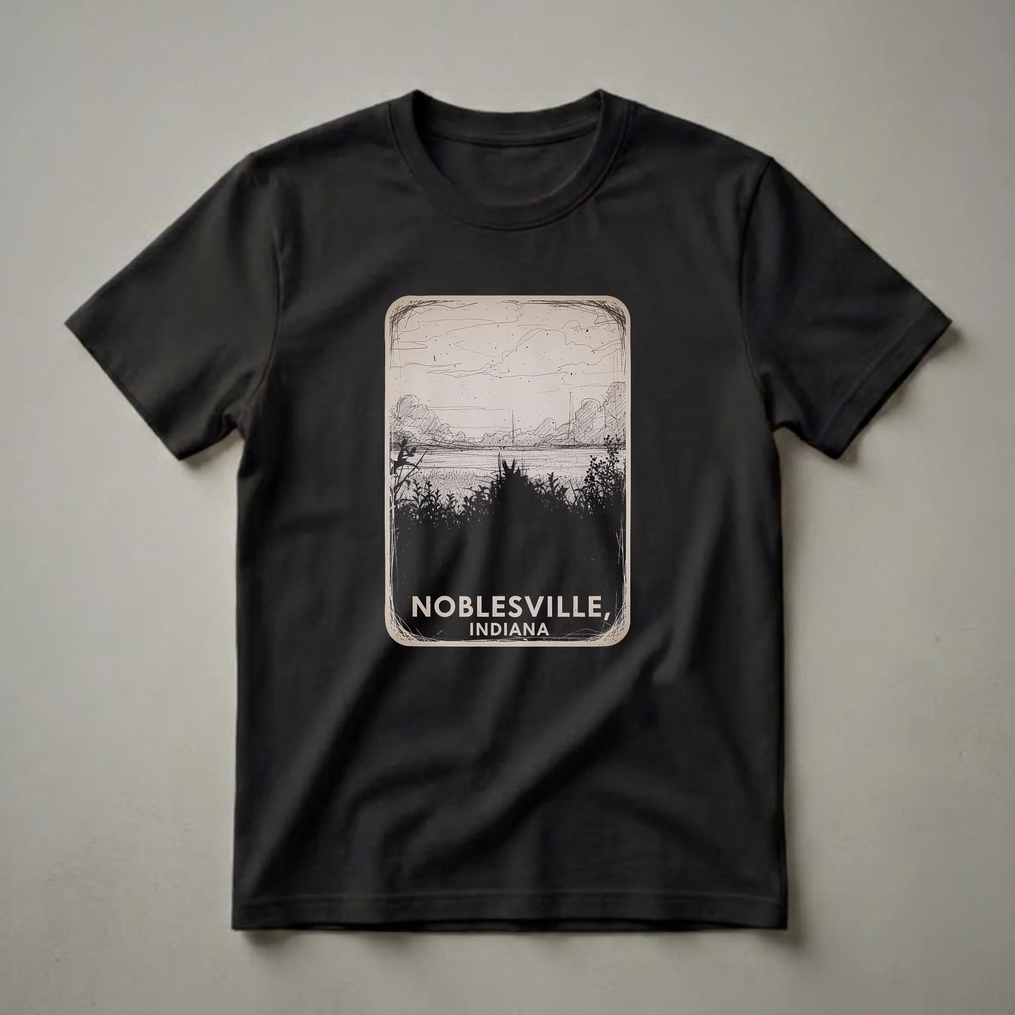 A vintage-style sketch graphic t-shirt featuring a landscape scene of Noblesville, Indiana with silhouetted foliage in the foreground and text at the bottom.