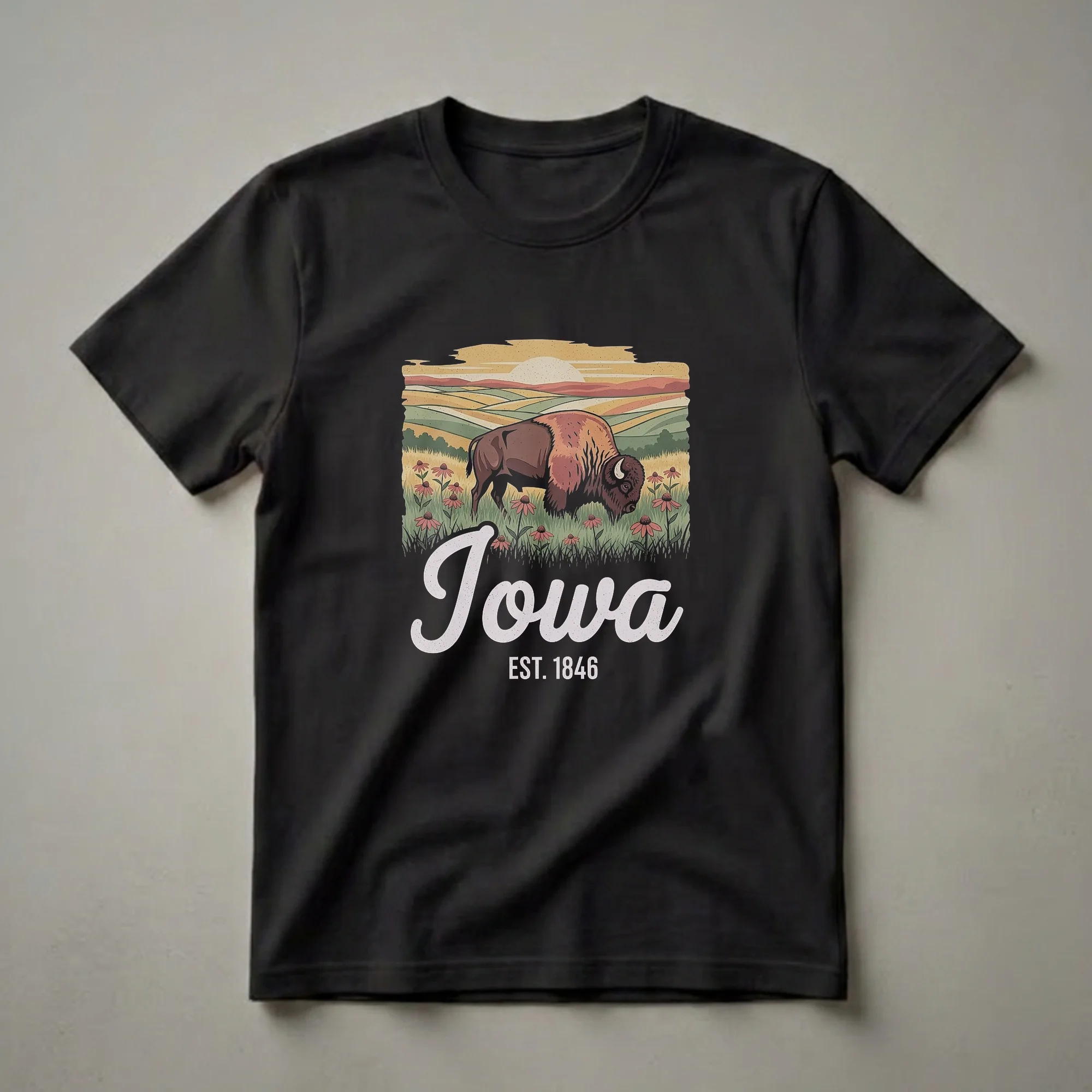 Black t-shirt featuring a retro graphic design of a bison in a field of coneflowers with rolling hills and a sunset, and the text 'Iowa Est. 1846'.