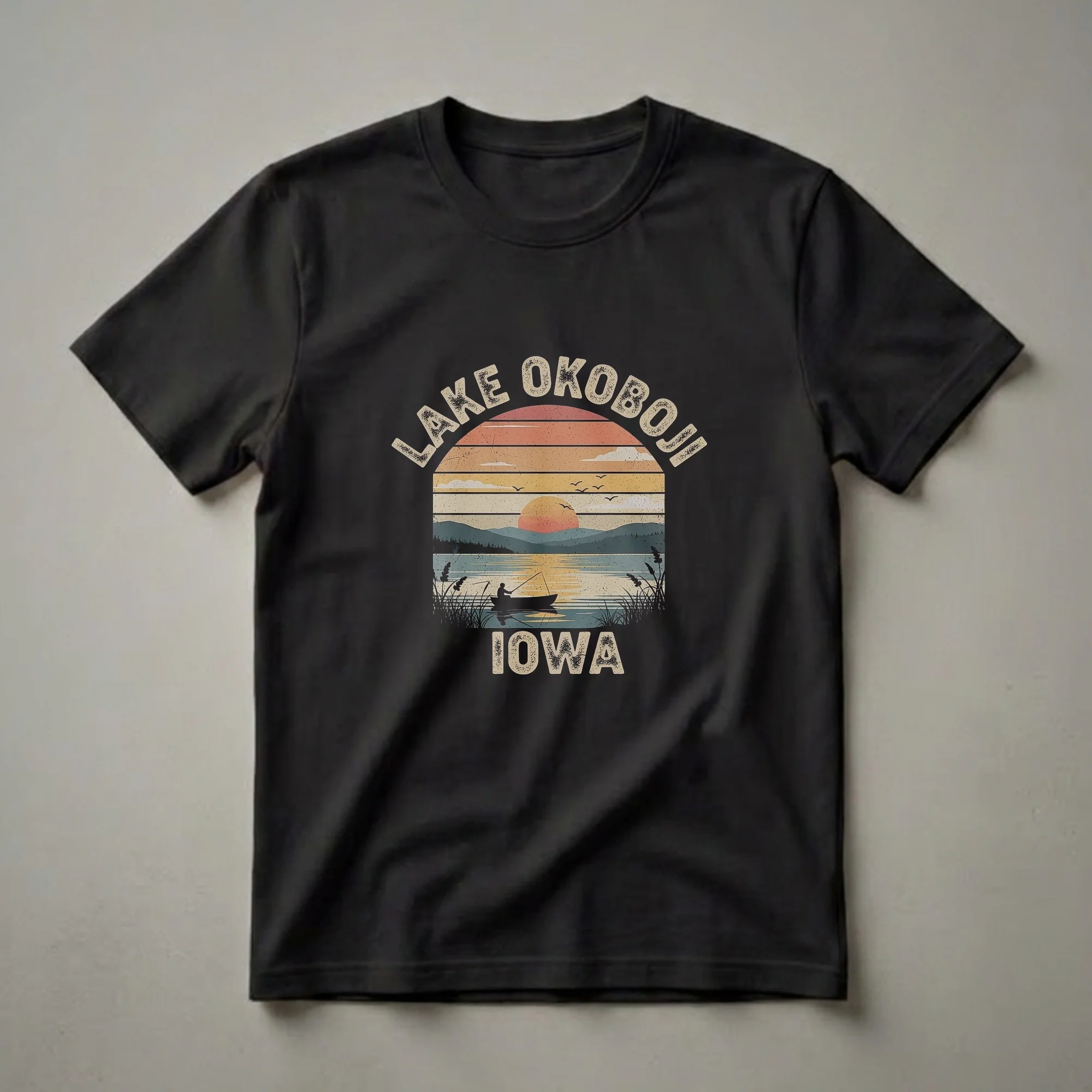Black t-shirt featuring a retro sunset graphic of Lake Okoboji, Iowa, with a fisherman in a boat, mountains, and text.