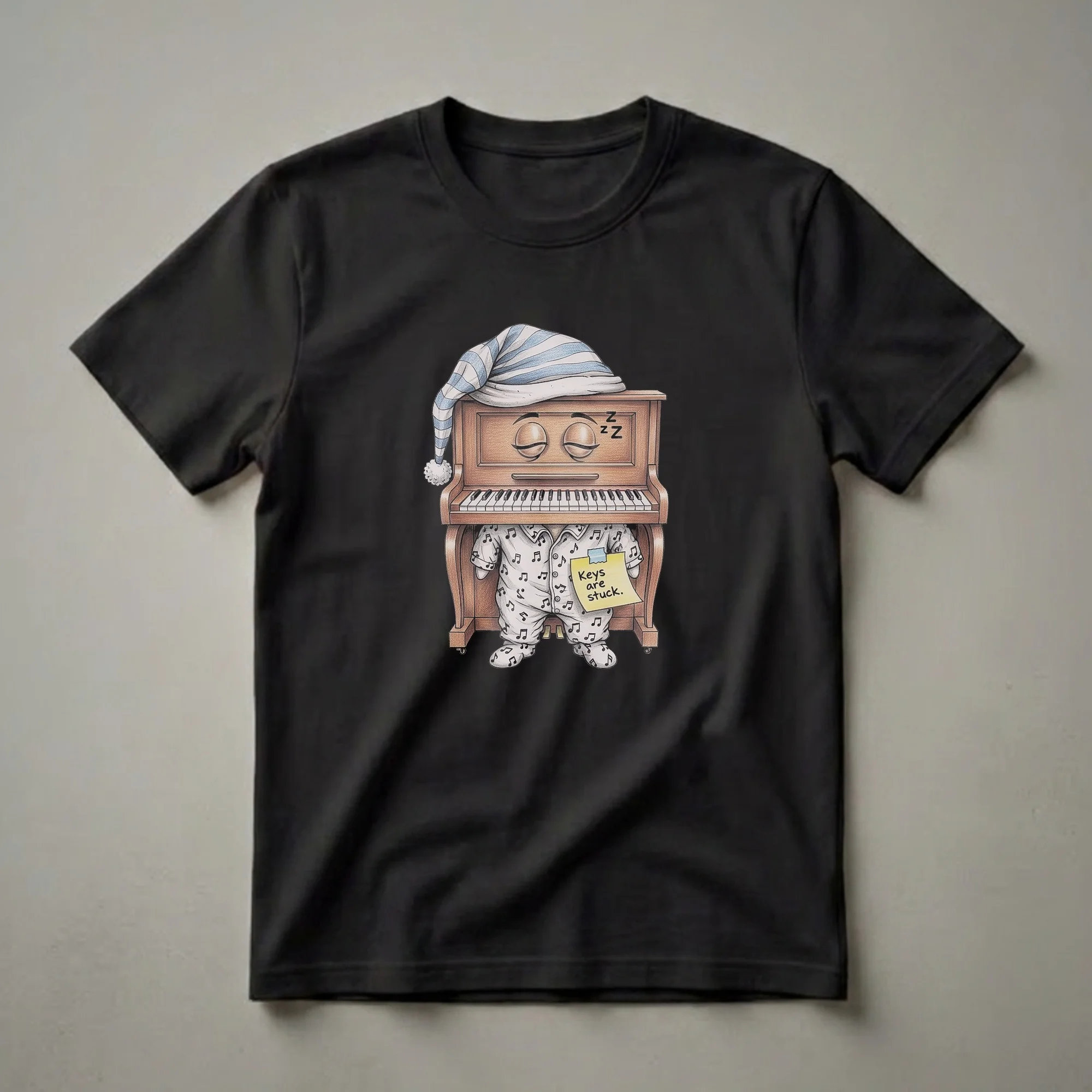 A graphic t-shirt featuring a whimsical illustration of a brown grand piano wearing striped pajamas and a sleeping cap, with a note that reads 'Keys are stuck.'