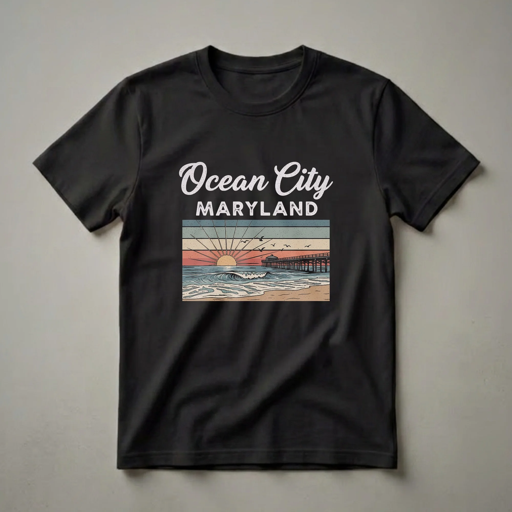 Black t-shirt with a retro graphic design of Ocean City, Maryland, featuring a sunset over the ocean, a wooden pier, rolling waves, seagulls, and colorful horizontal stripes.