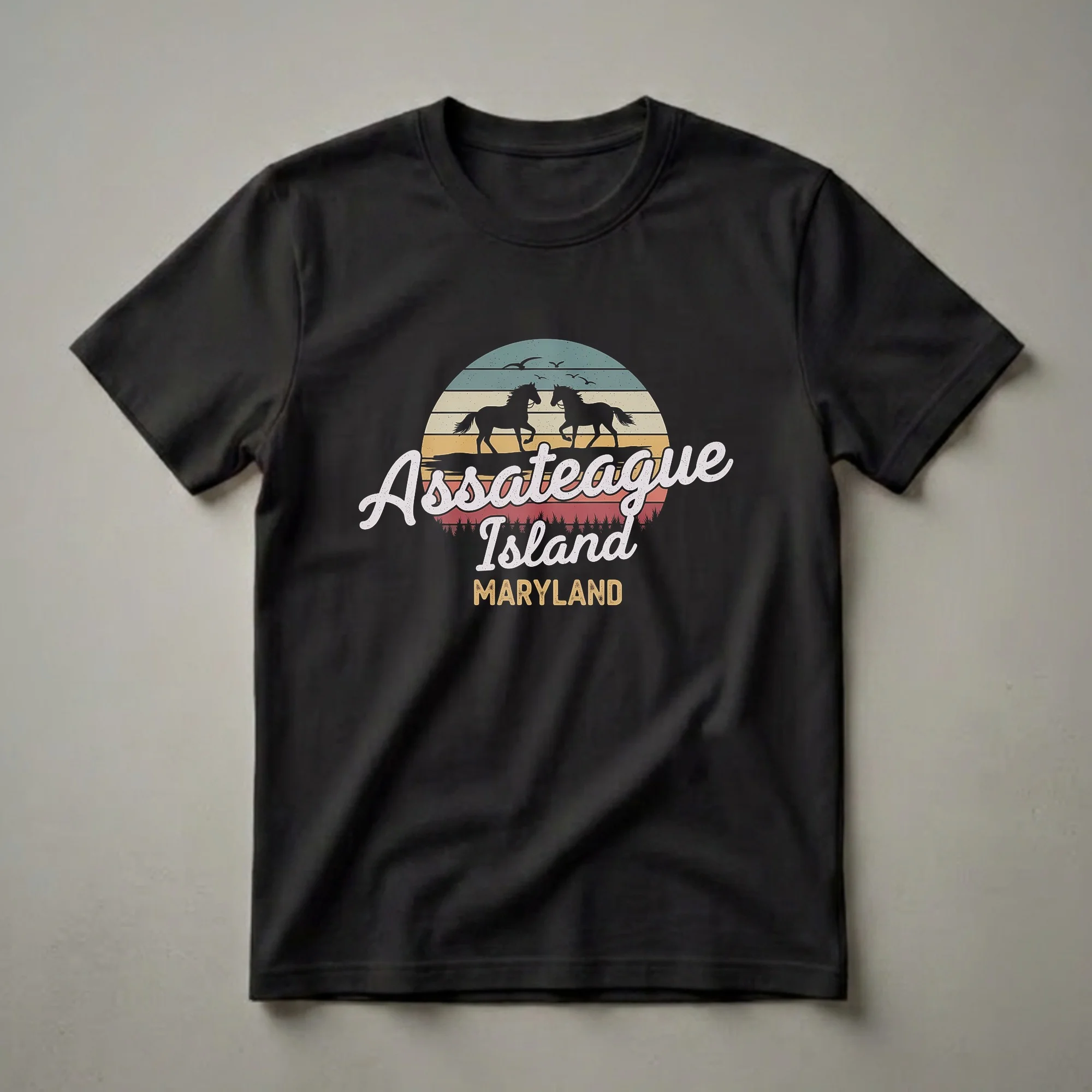 Black t-shirt with a retro sunset graphic featuring two silhouetted horses, seagulls, and the text 'Assateague Island Maryland'.
