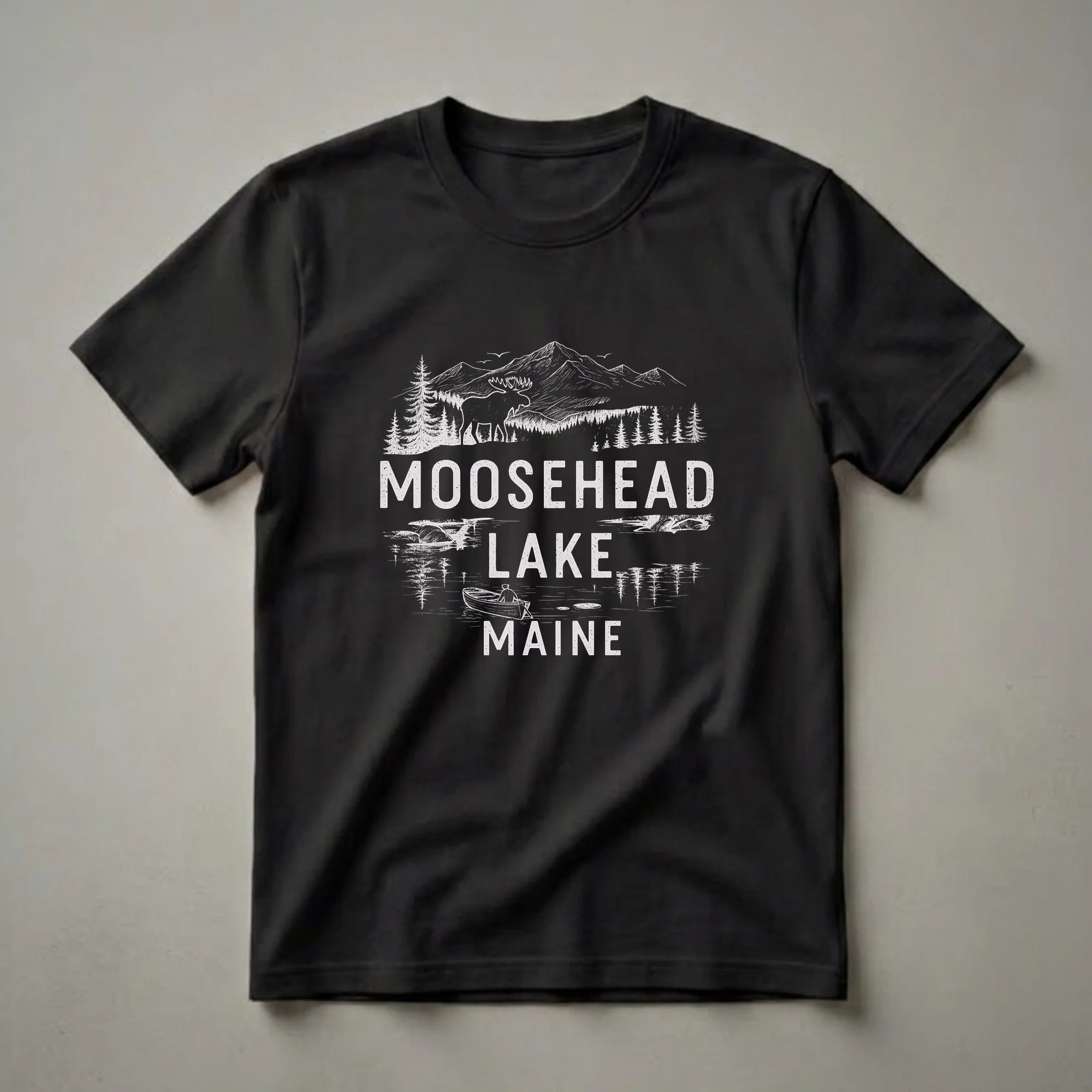 Black t-shirt with a white graphic design of Moosehead Lake, Maine, featuring a moose, pine trees, mountains, and a person in a rowboat.
