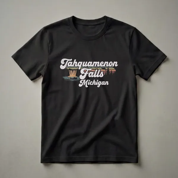 Black t-shirt with a retro graphic design featuring the words 'Tahquamenon Falls Michigan' over an illustration of waterfalls, a canoeist, a leaping fish, pine trees, and a sunset.