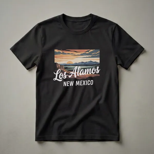Black t-shirt with a retro graphic design depicting a sunset landscape over Los Alamos, New Mexico, featuring mesas, water, and mountains.