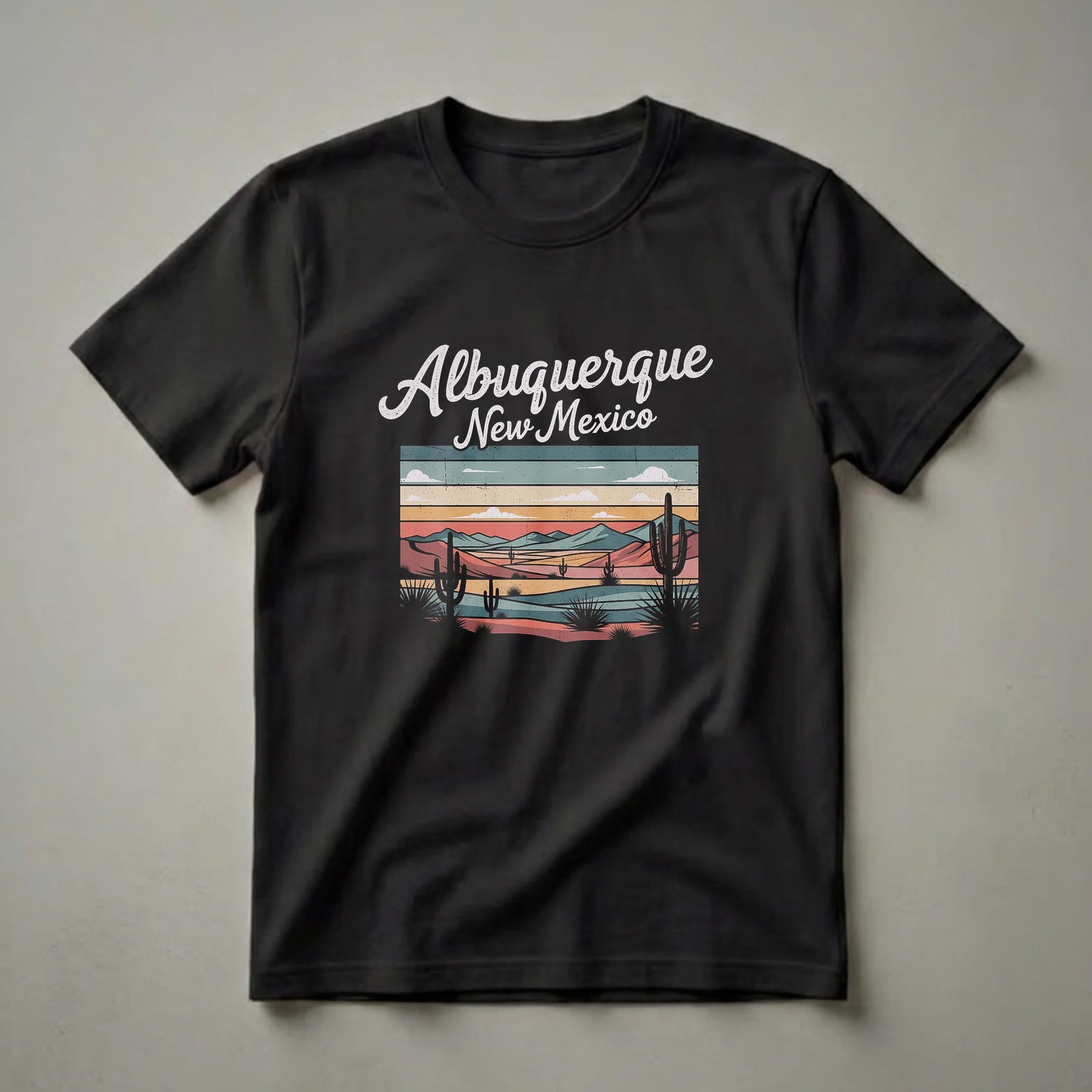 Black t-shirt with a retro graphic design of Albuquerque, New Mexico, featuring a desert landscape with saguaro cacti, mountains, and a sunset color palette.